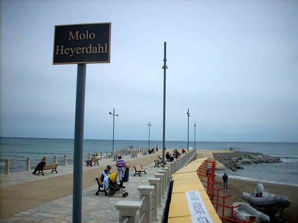 Molo Heyerdahl sign, people sitting on benches along the pier under grey sky