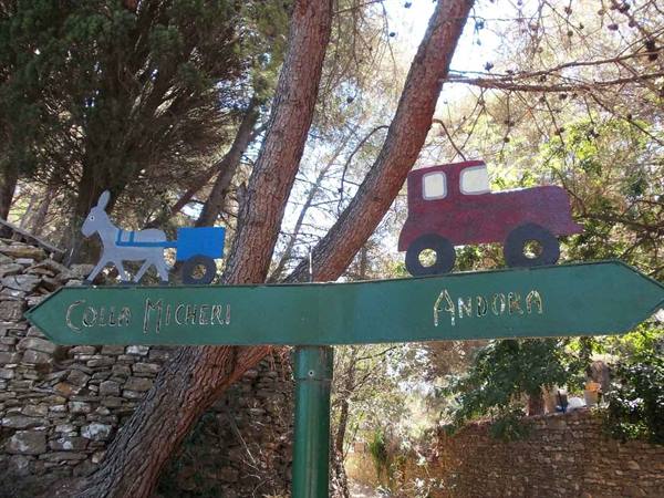 Green metal sign with painted donkey and car, directions to Colla Micheri and Andora