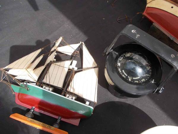 Wooden model sailing ship with white sails next to a black compass