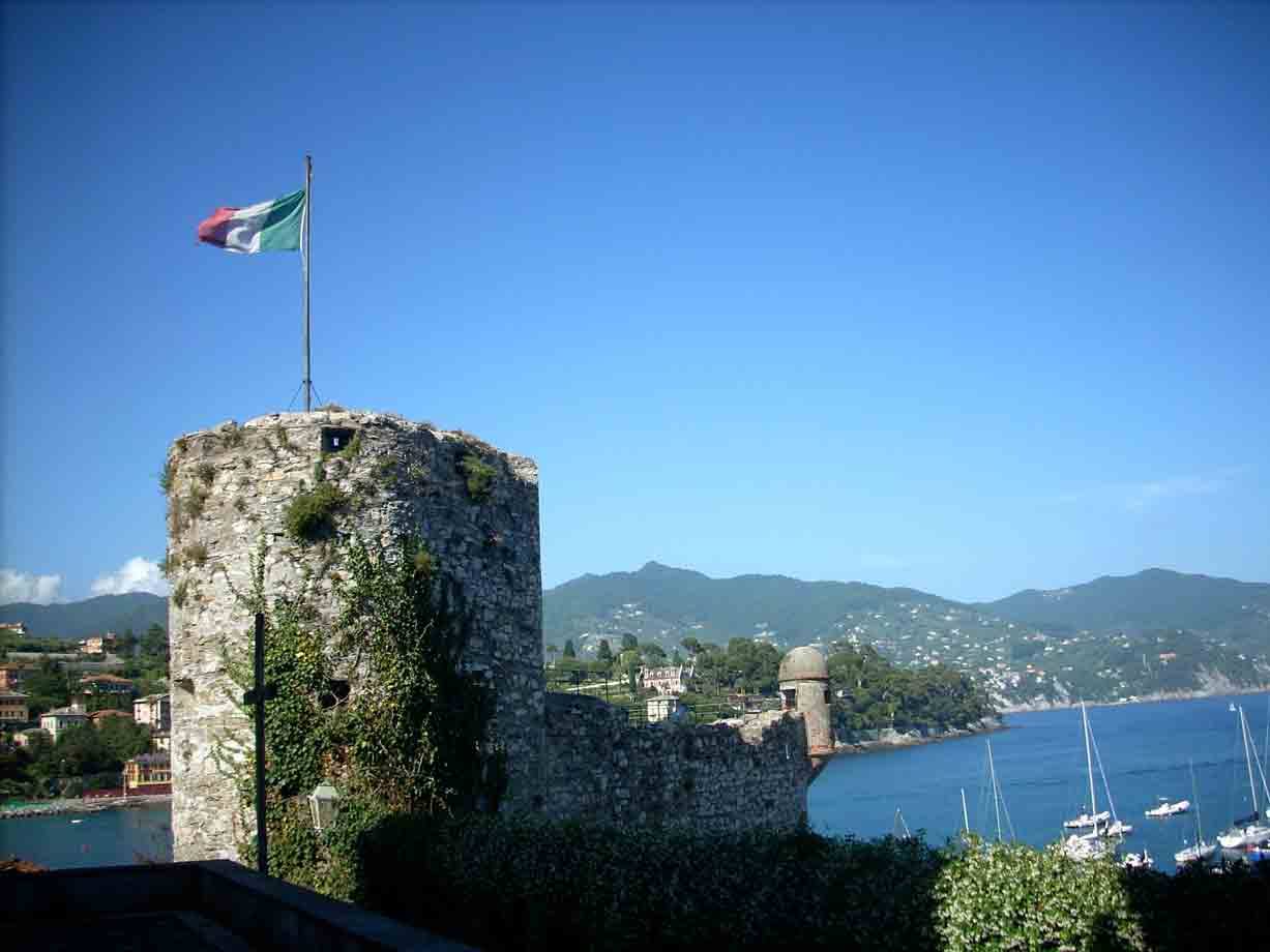 Torre di pietra del castello di Rapallo con bandiera italiana e barche