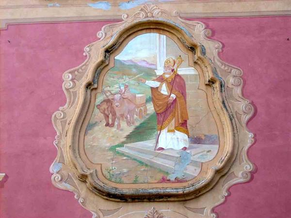 Fresco of a bishop saint with staff and oxen, framed in stucco on pink wall