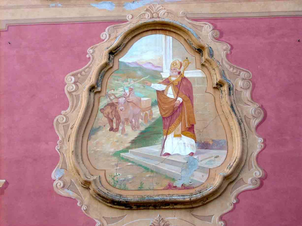Affresco di santo vescovo con bastone e buoi, incorniciato in stucco su muro rosa