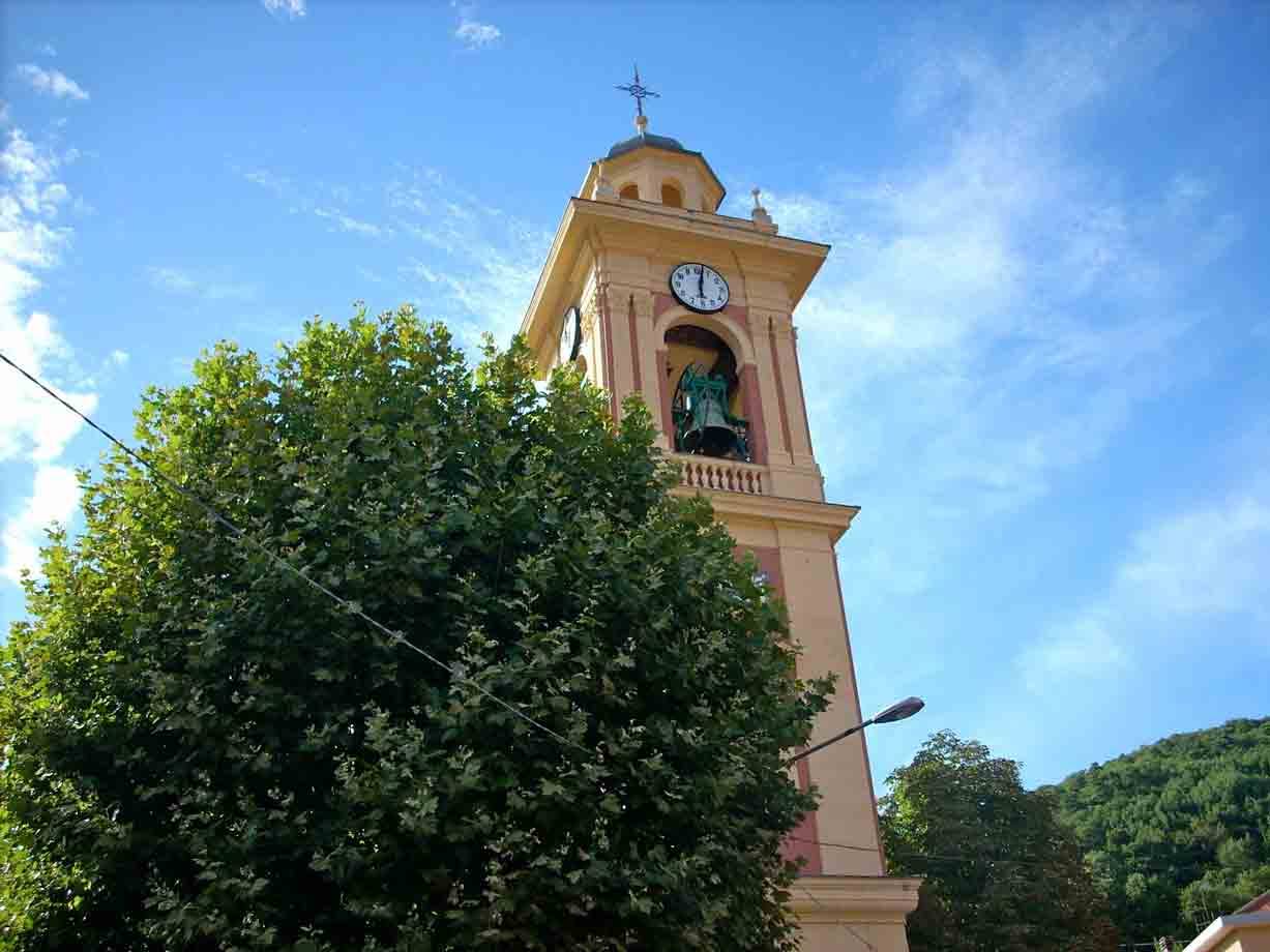 Campanile giallo con orologio e campana sopra gli alberi verdeggianti