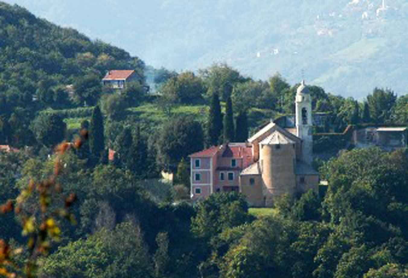 Chiesa con campanile tra case rosse sul colle verde, colline nebbiose