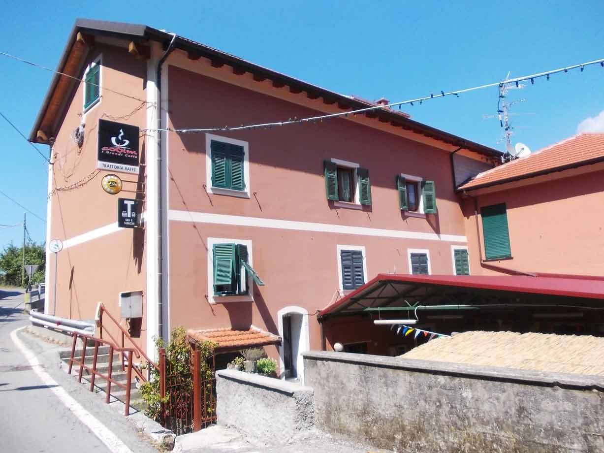 Trattoria con insegna nera su casa rosa con persiani verdi, cielo azzurro