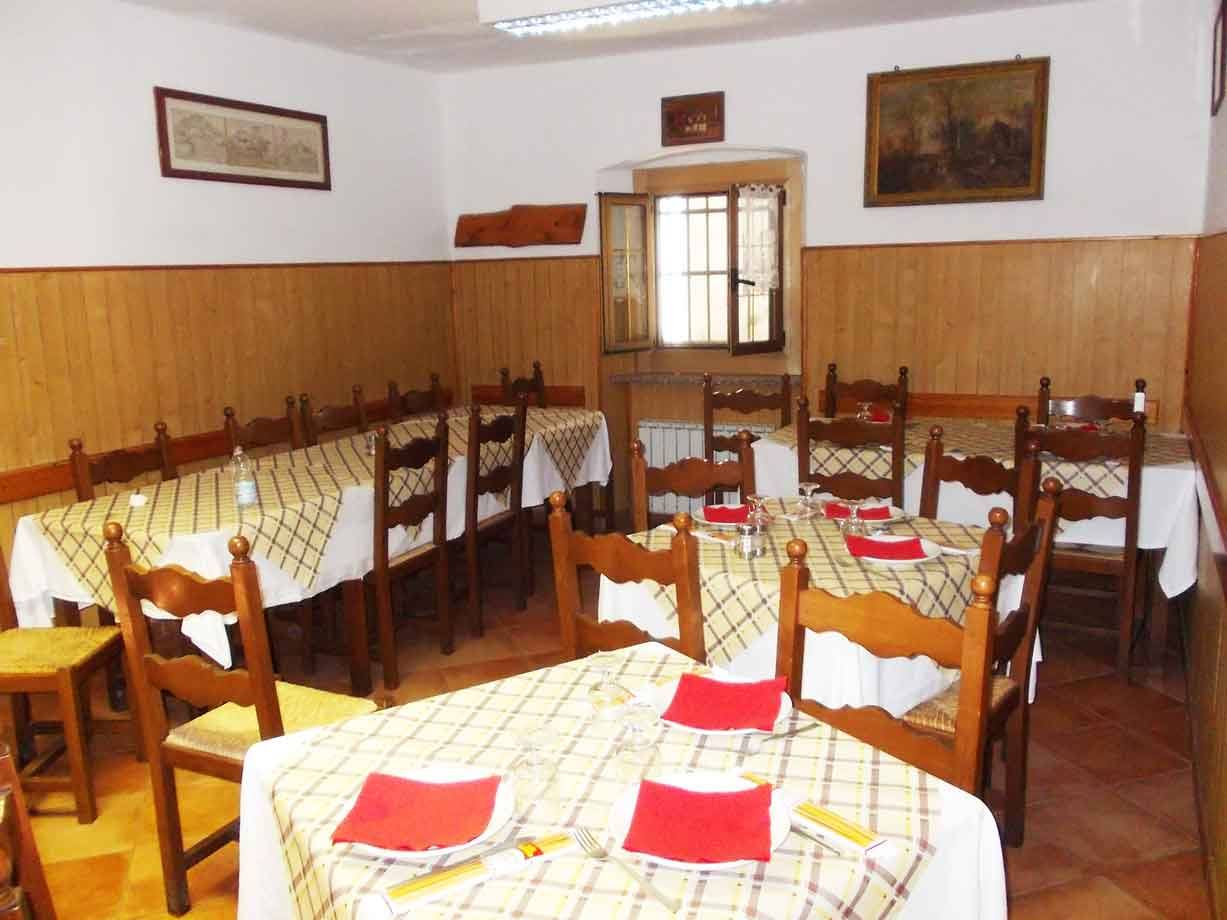Sala trattoria con tavoli apparecchiati, tovaglie a quadri, sedie in legno e finestra illuminata