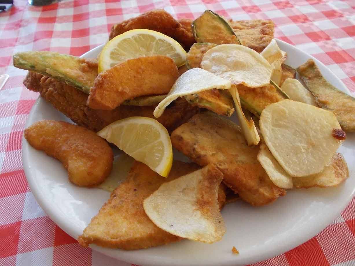 Piatto di fritto misto con zucchine, battute di merluzzo, patate chips e spicchi di limone
