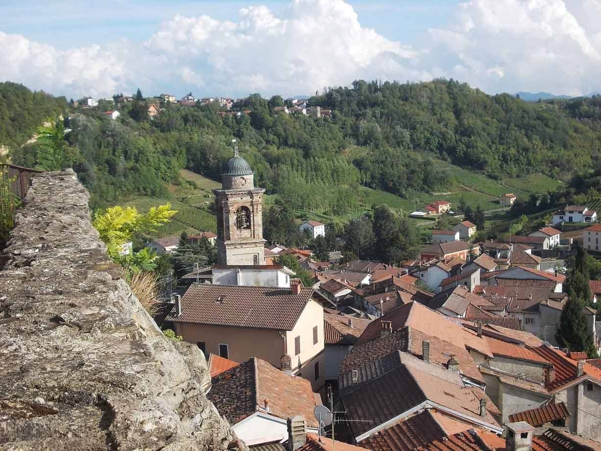 Campanile con cupola sopra tetti di terracotta tra colline verdi e case sparse