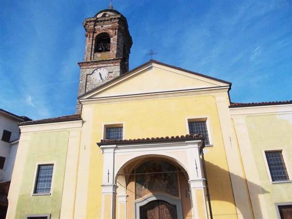 Yellow church facade with frescoed porch and old stone bell tower