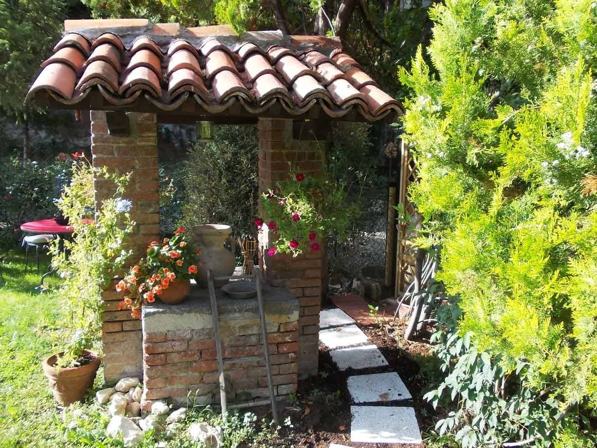 Pozzo in mattoni con copertura di tegole, fiori in vaso e vialetto di pietre
