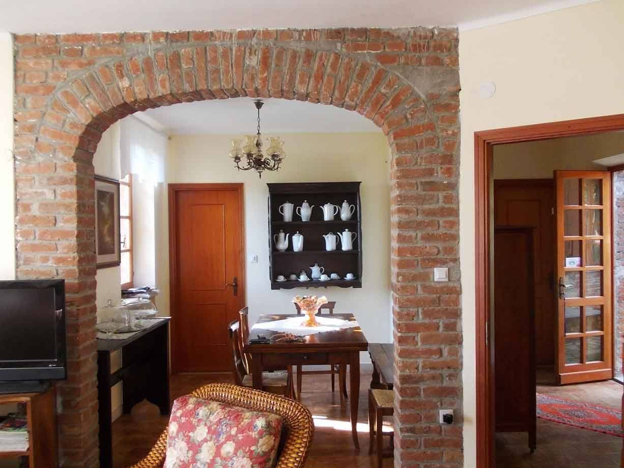 Arco in mattoni rossi verso sala da pranzo con tavolo, credenza nera e teiere bianche