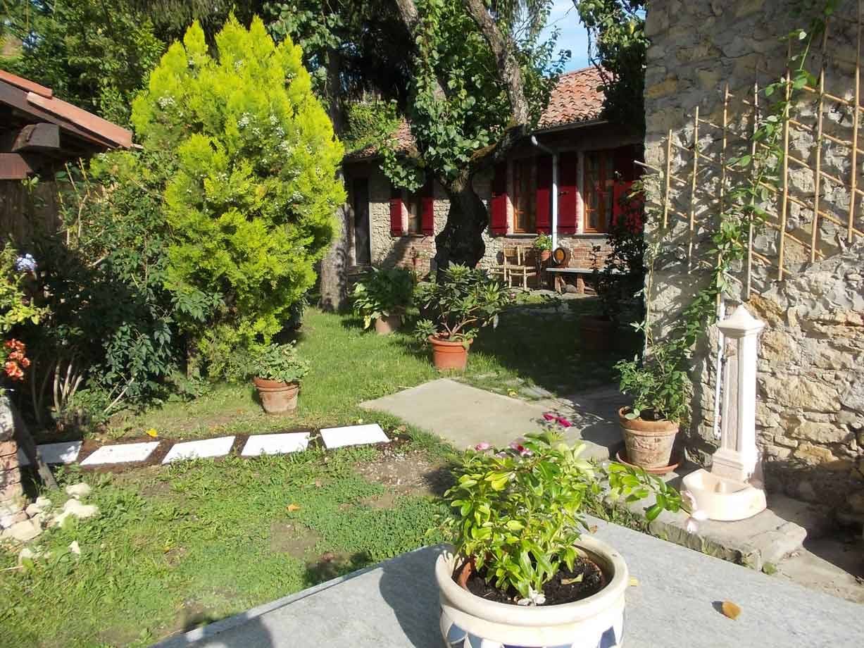 Giardino con vasi di fiori, pietre bianche e casa rurale in pietra con tetti rossi