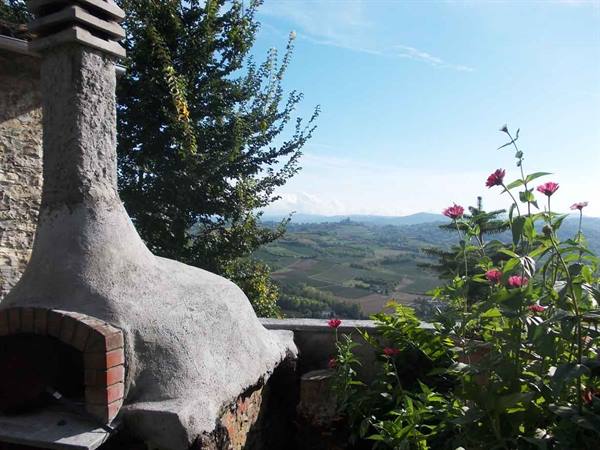 Stone and cement wood-fired oven with pink flowers and farmed hills beyond