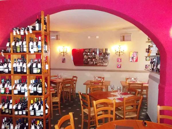 Wine bottle rack and wooden tables inside pink-walled Italian trattoria
