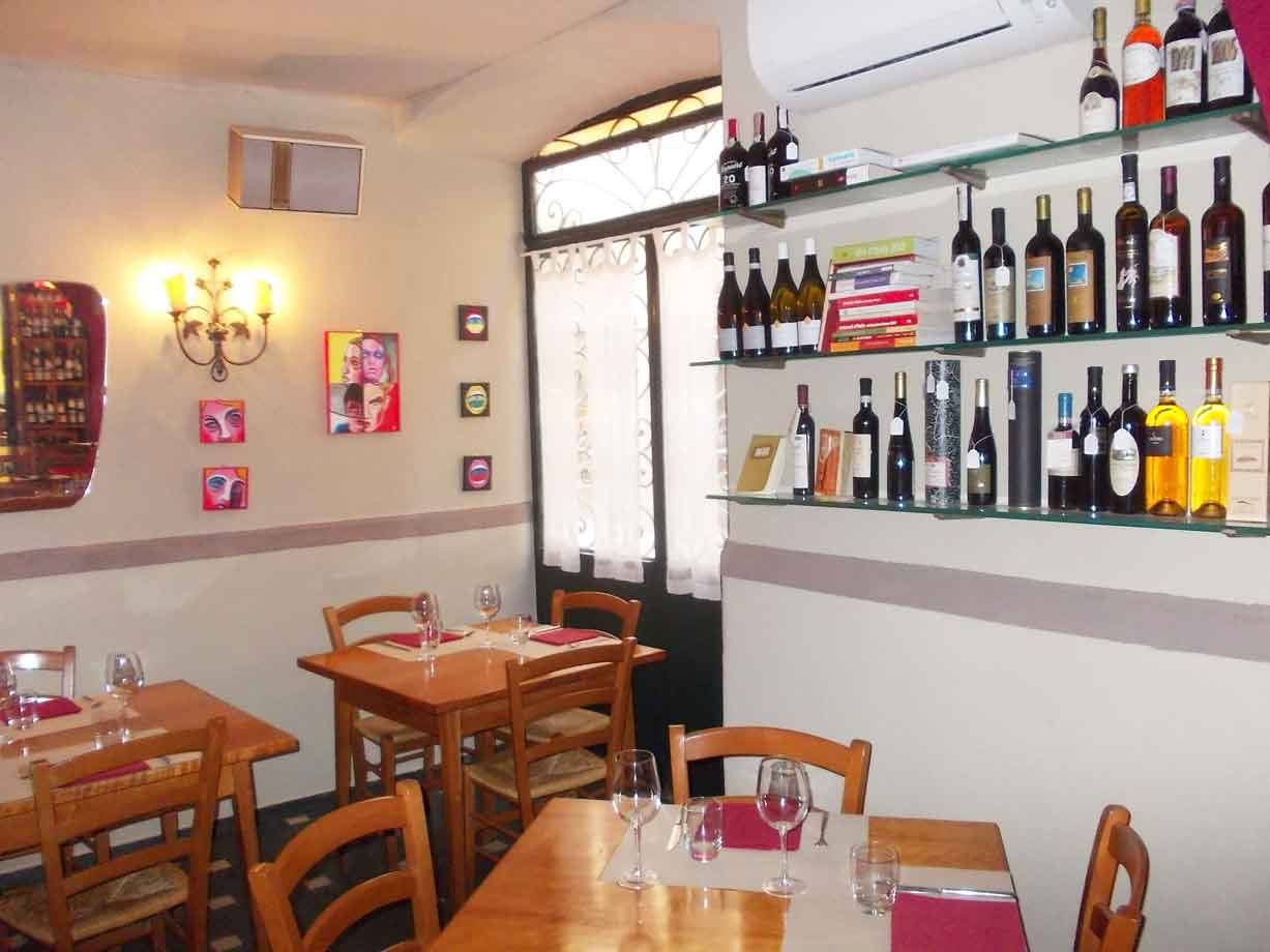 Sala di trattoria con tavoli in legno, bicchieri e bottiglie di vino su mensole
