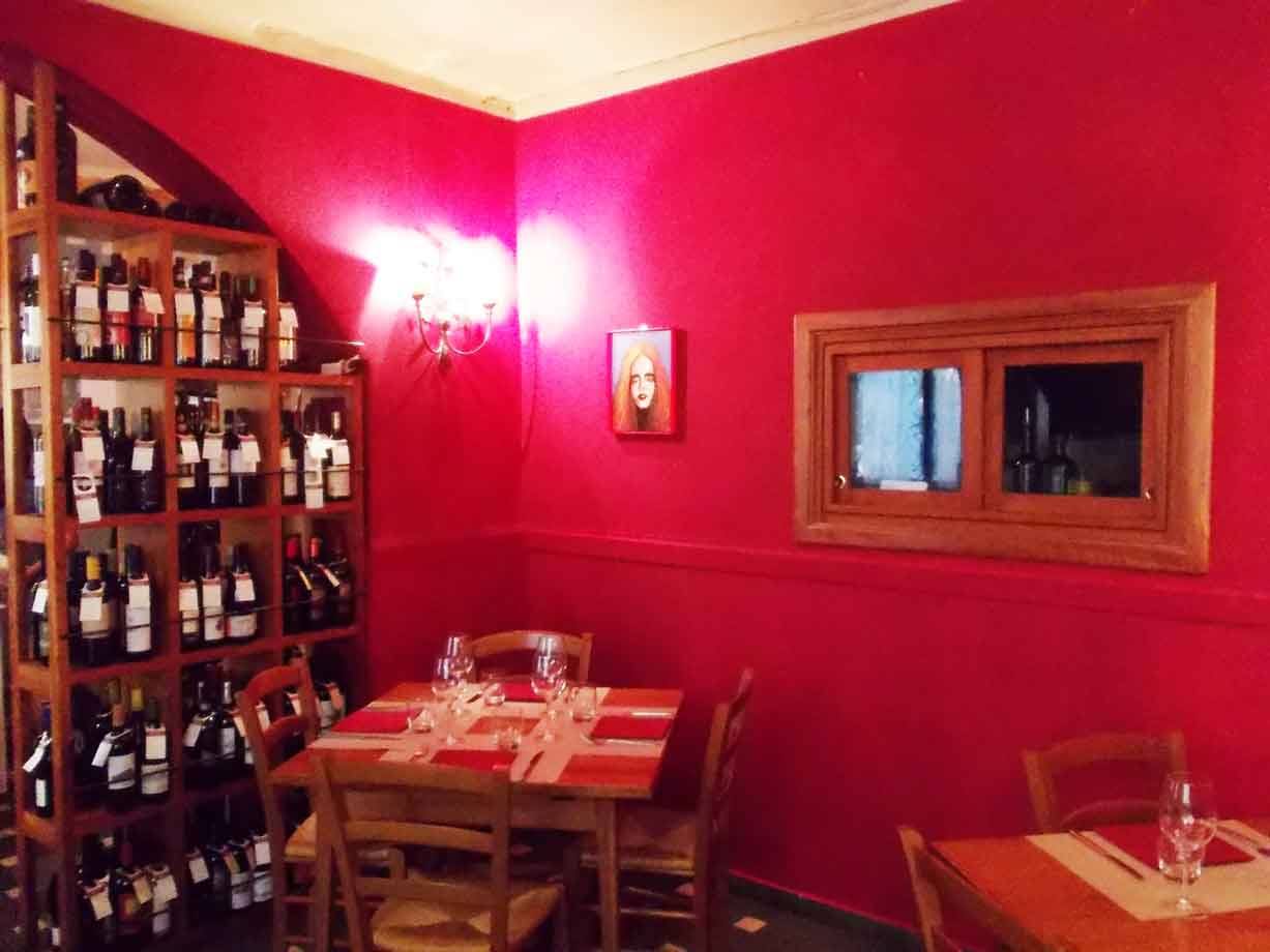 Sala di trattoria con pareti rosse, bottiglie di vino in legno e tavole apparecchiate