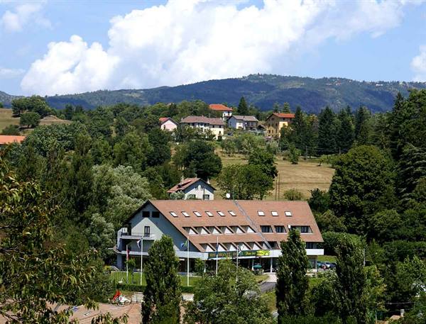 Sloped-roof hotel among trees and scattered houses on wooded hills