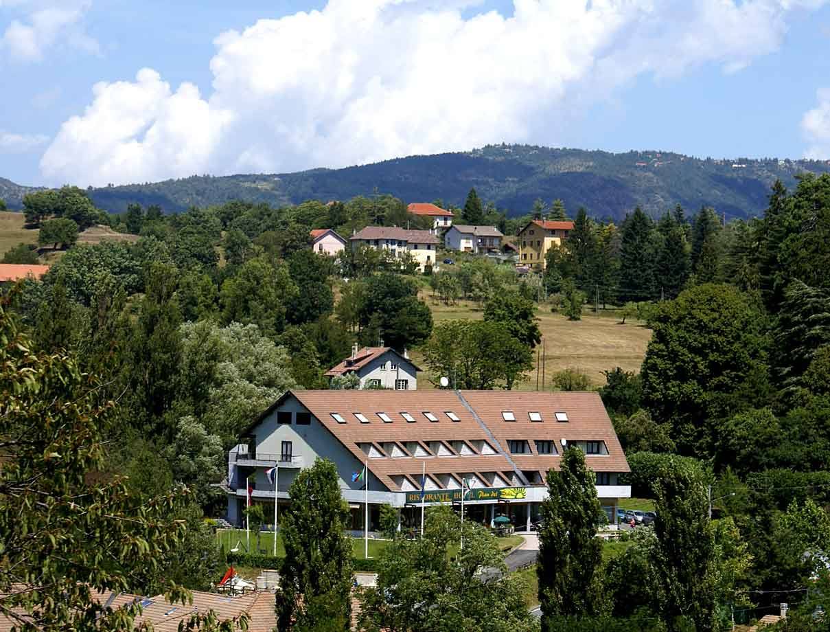 Albergo con tetto spiovente tra alberi e case sparse sui colli boscosi
