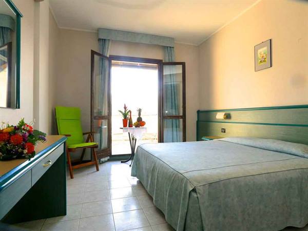 Hotel room with blue bed, green armchair and open balcony door