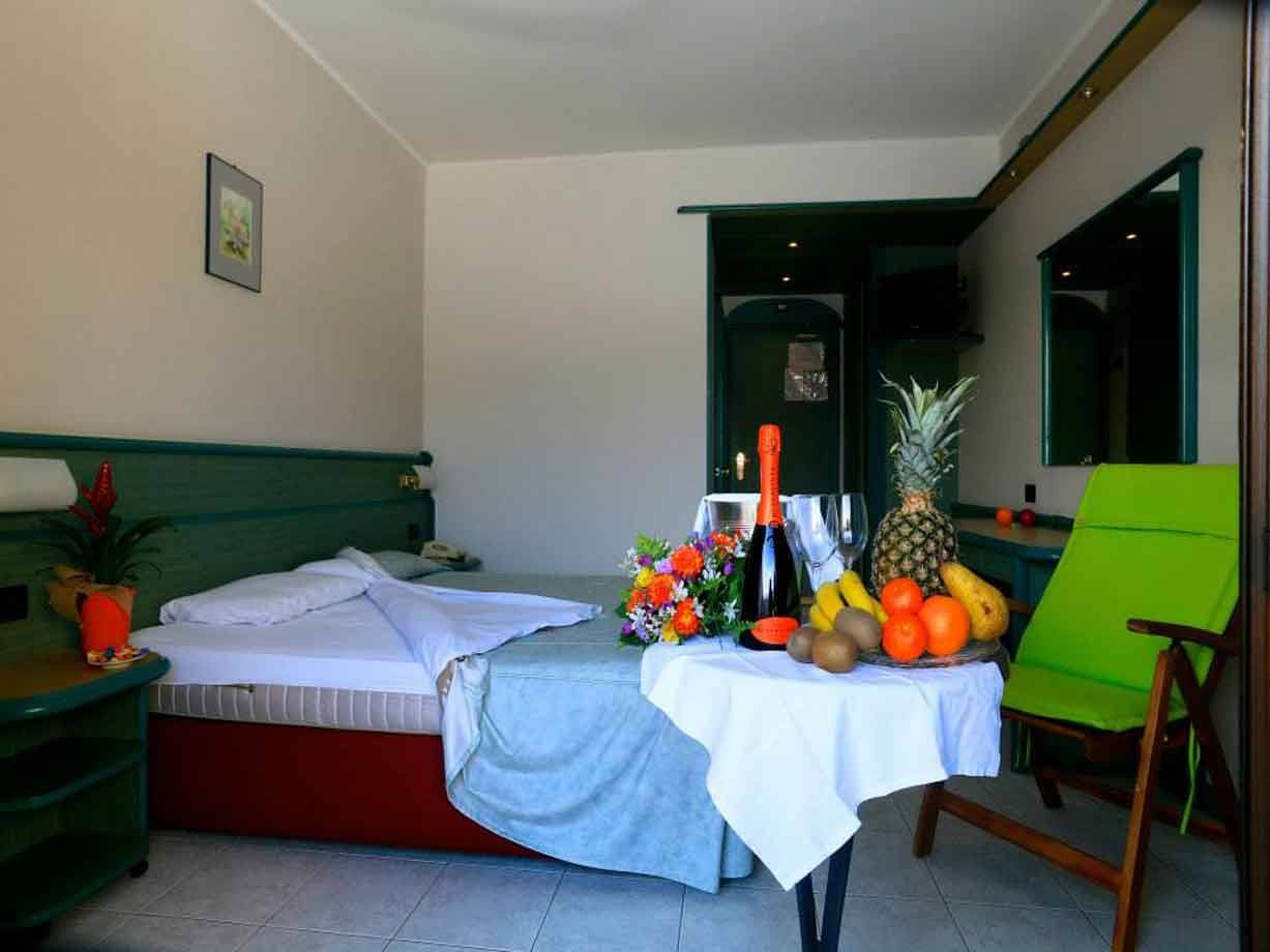 Camera d'albergo con letto, bottiglia di spumante, frutti tropicali e fiori