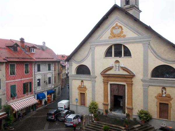 Ochre church facade with steps, colorful houses and parked cars in square