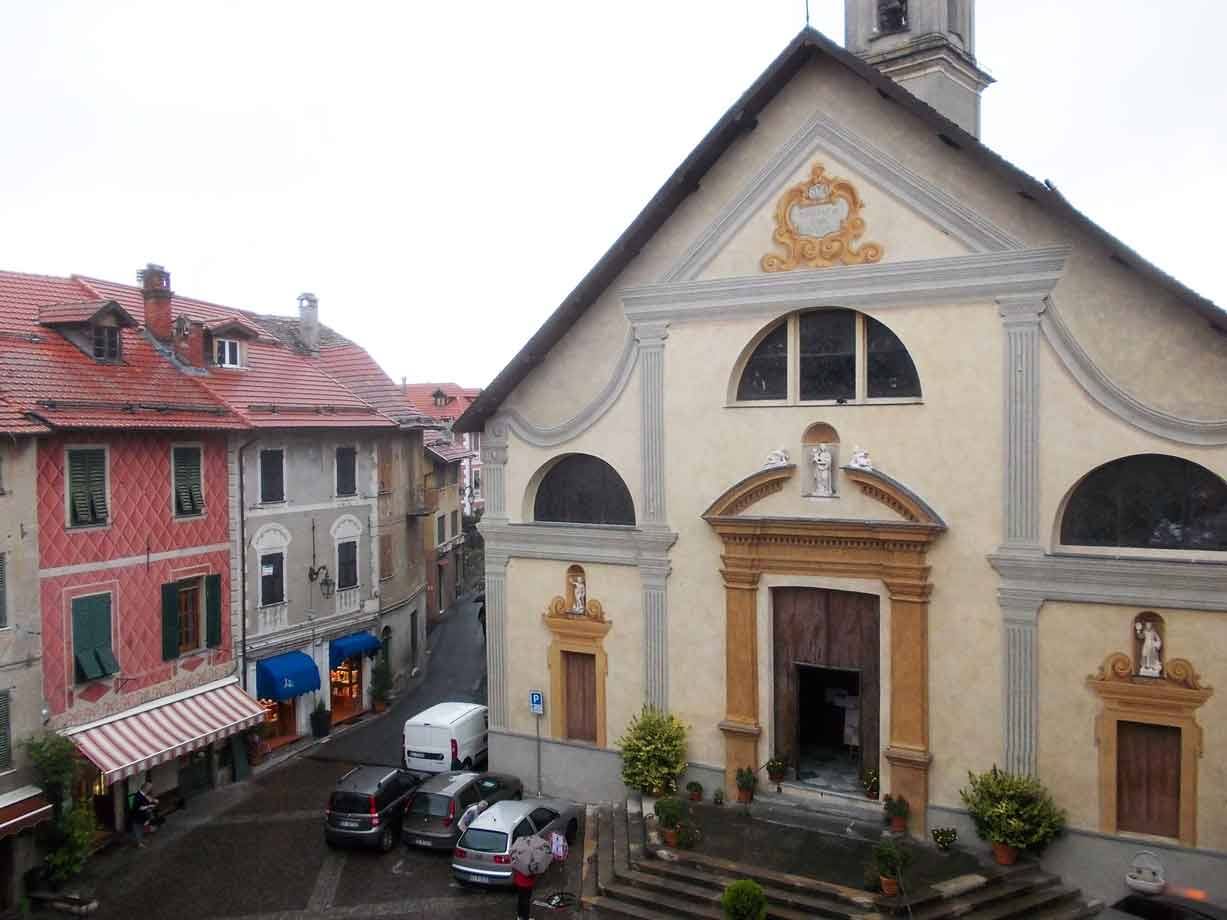 Chiesa con facciata ocra e scalinata, case colorate e auto in piazza