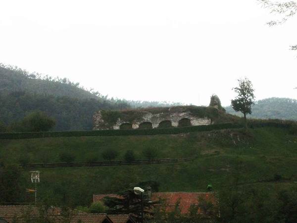 Stone wall ruin with arches on green hill, rooftops below