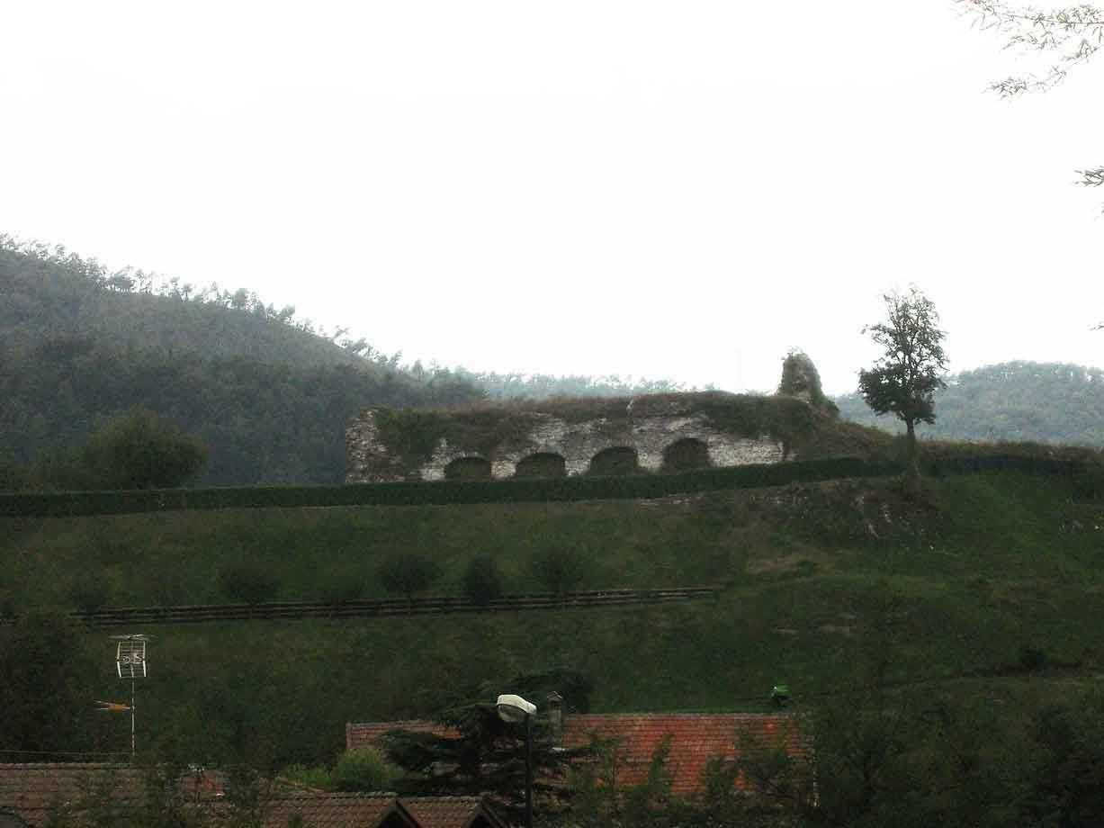 Rovina di muro con archi su collina verde, tetto in primo piano