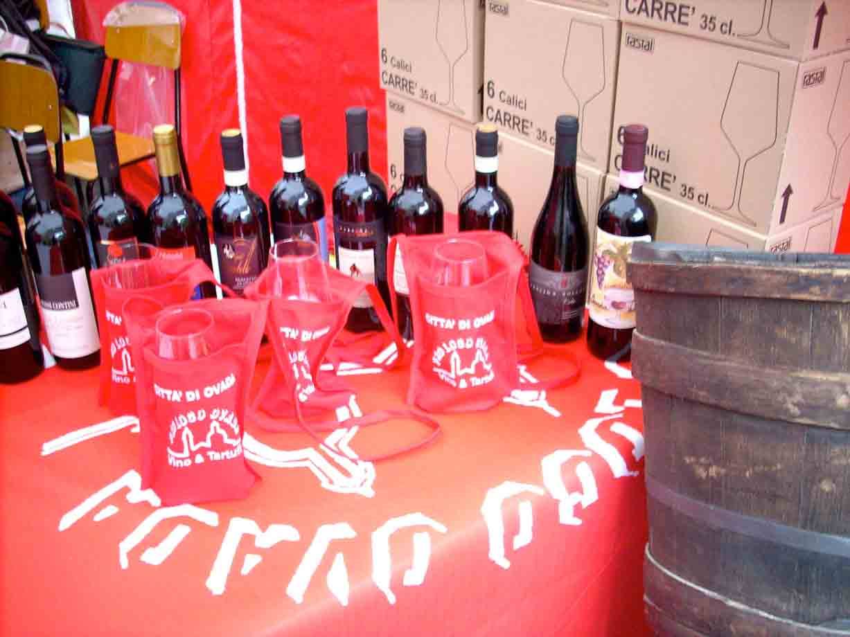 Bottiglie di vino su tavolo rosso, calici in sacchetti rossi, barile di legno e scatole