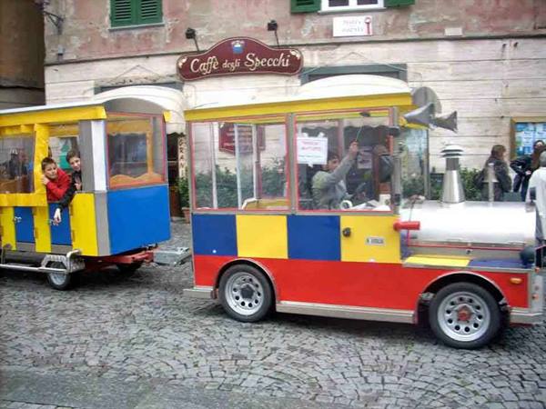 Colorful tourist train with children aboard in front of Caffè degli Specchi
