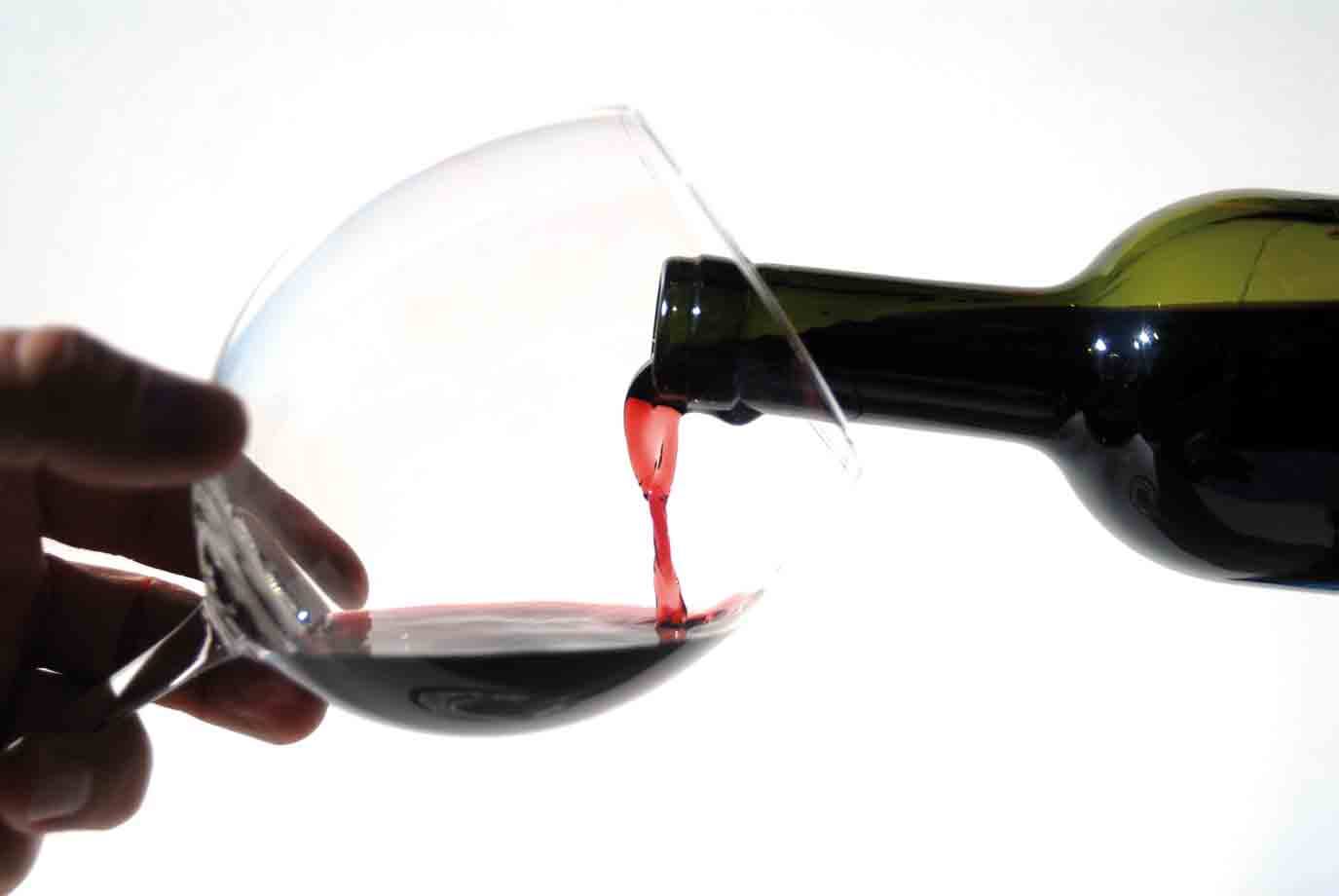 Rovesciato vino rosso da bottiglia verde in calice tenuato su sfondo bianco