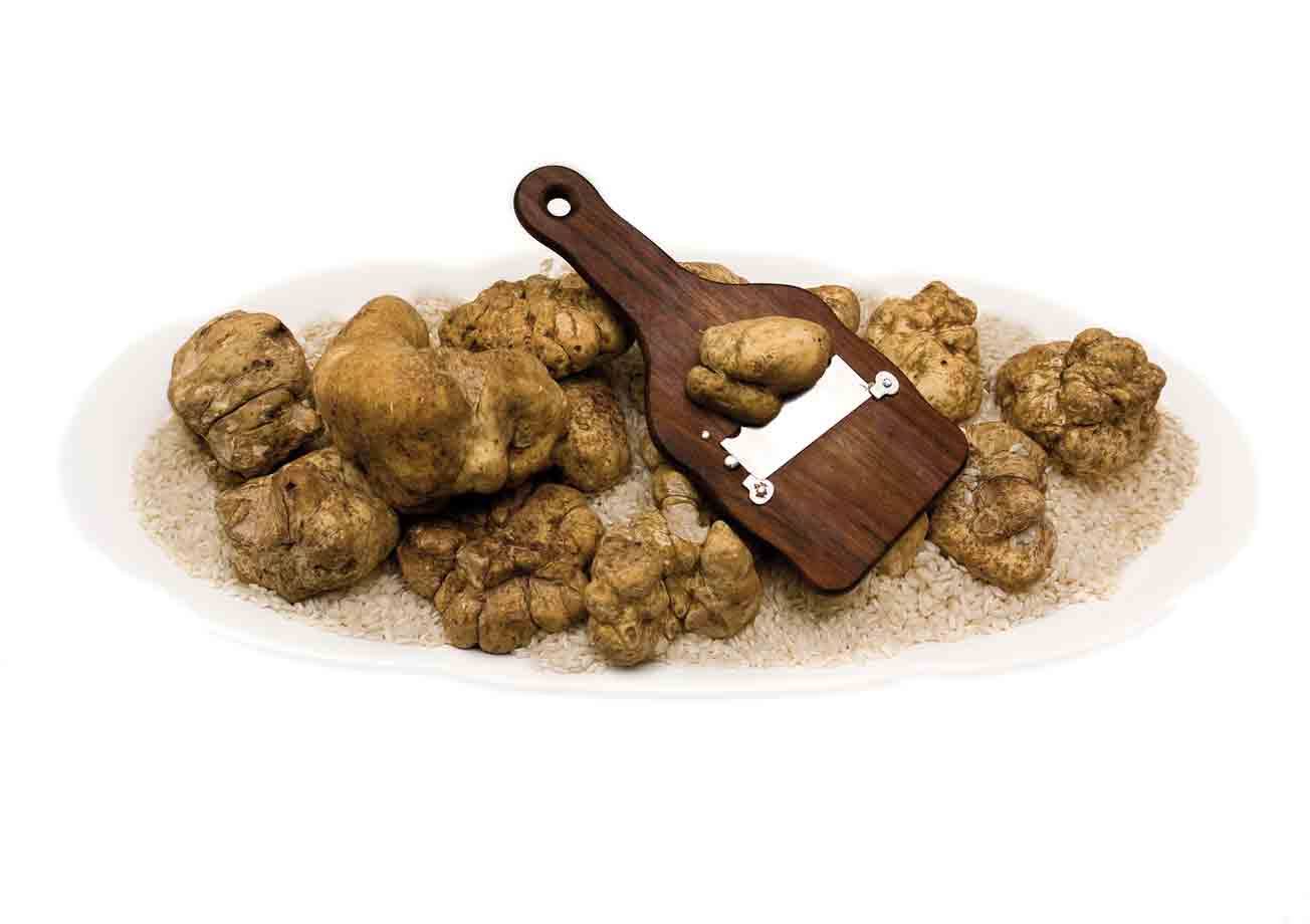 Tartufi bianchi su piatto di riso con tagliatartufi in legno