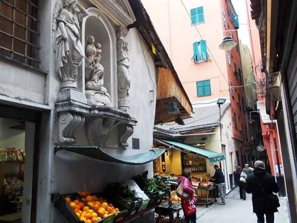 Alley with marble votive shrine and fruit stall, people shopping among colorful houses