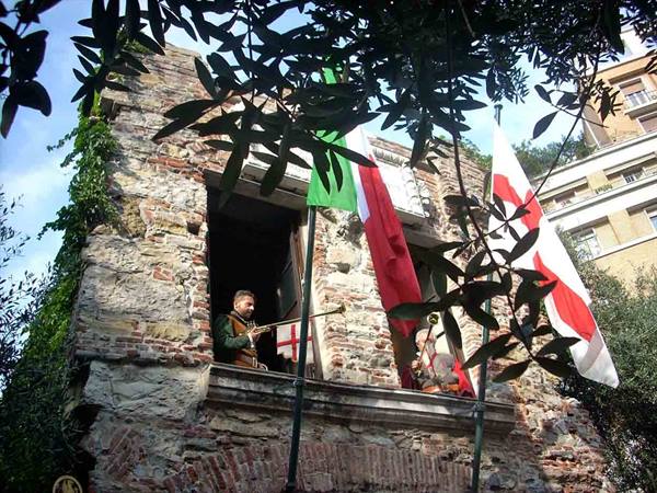 Trumpeter plays from the window of an old stone house with flags, Genoa