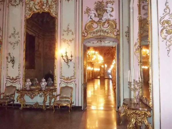 Baroque hall with gilded stuccoes, mirrors and doorway to chandelier-lit gallery