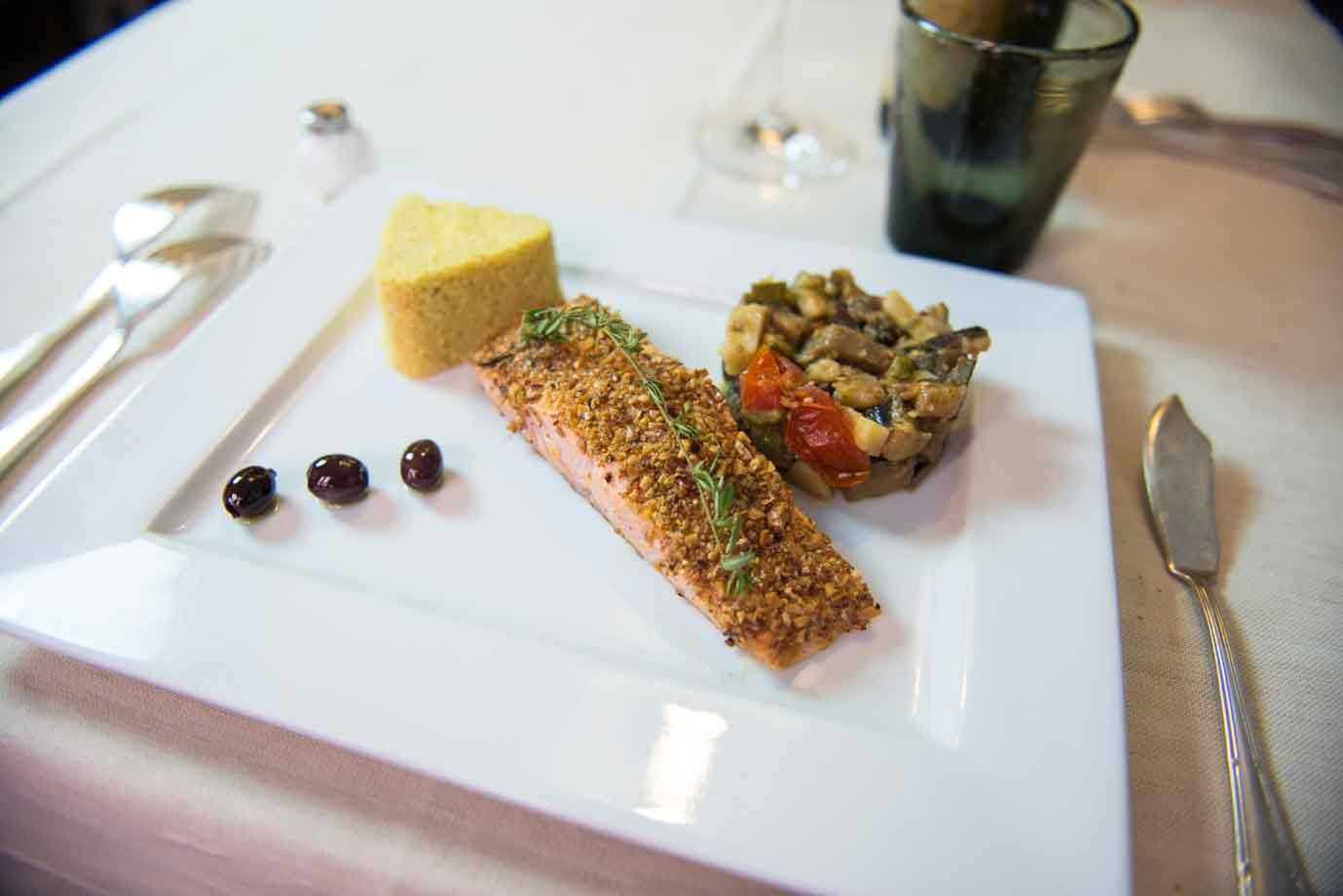 Piatti bianco con salmone croccante, polenta e caponata, tre olive