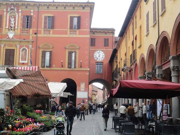 Street market under arcades: flower stall, clock on arch, pedestrians