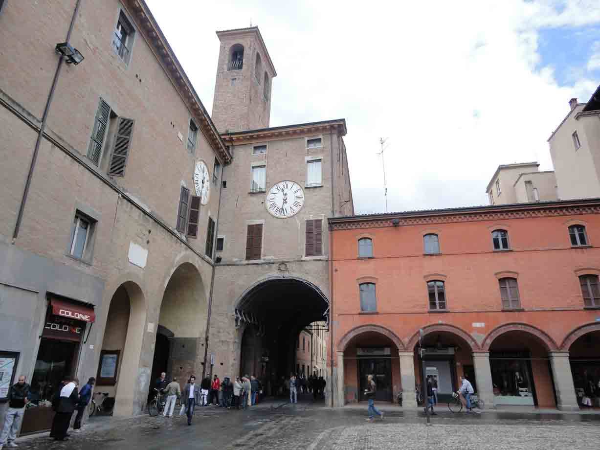 Turisti passano sotto l'arco di un antico palazzo con torre e orologio