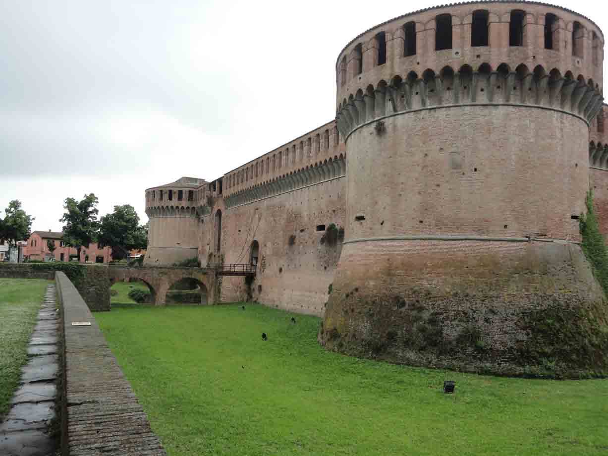 La Rocca di Imola: mastio circolare in mattoni sotto cielo grigio, prato bagnato
