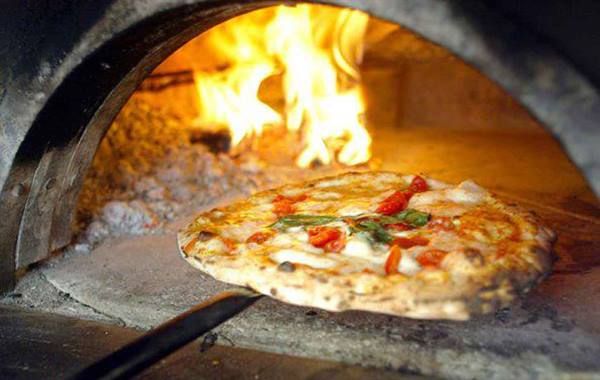Margherita pizza on a peel inside a wood-fired oven with flames