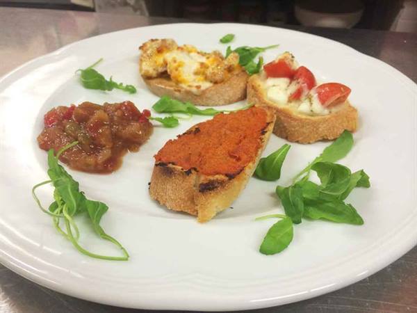 White plate with tomato bruschettas, red spread and arugula leaves