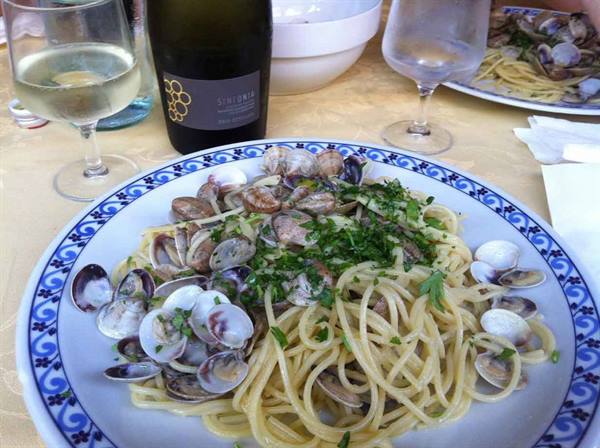 Spaghetti with clams and parsley on a decorated plate, white wine and bottle on yellow tablecloth