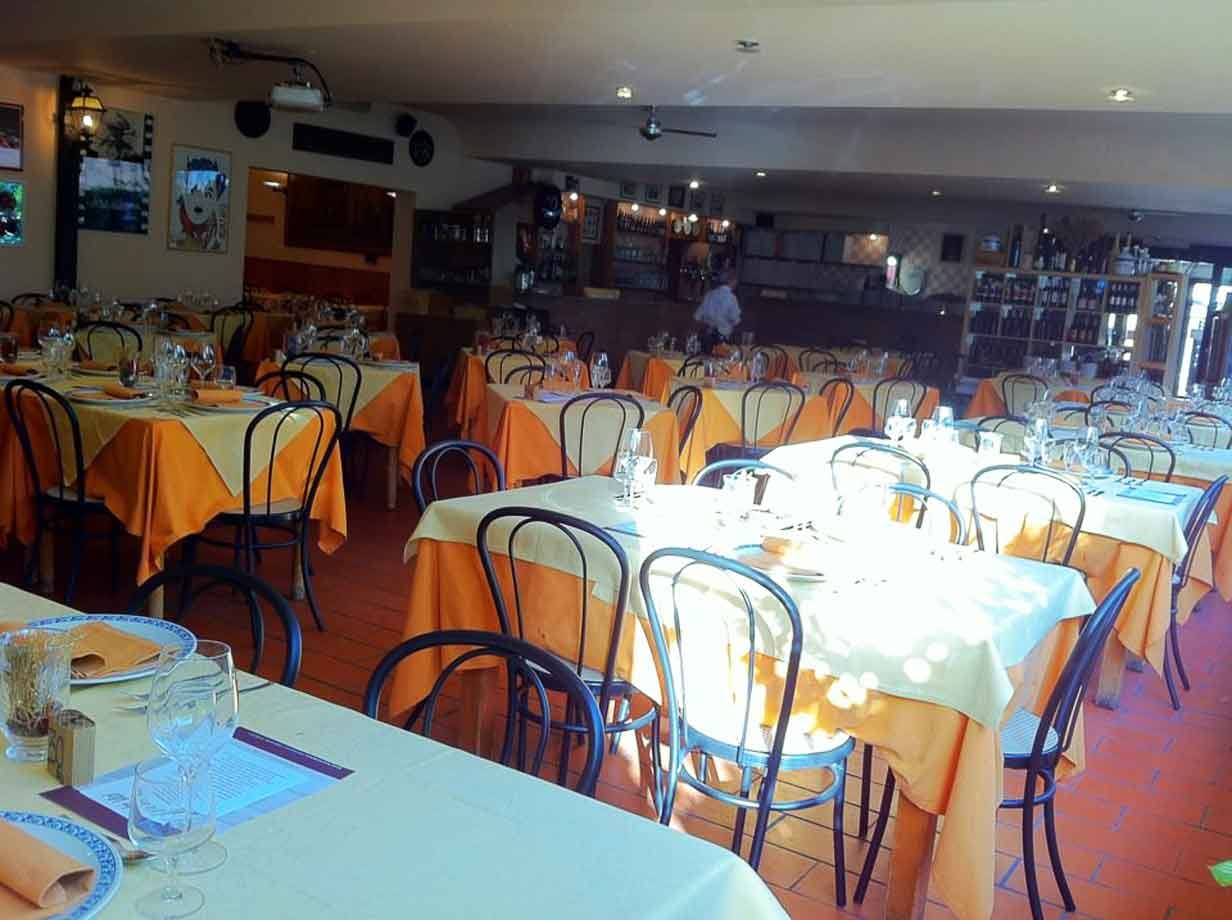 Sala di ristorante apparecchiata, tavoli con tovaglie gialle e arancioni, sedie thonet, luce del mattino