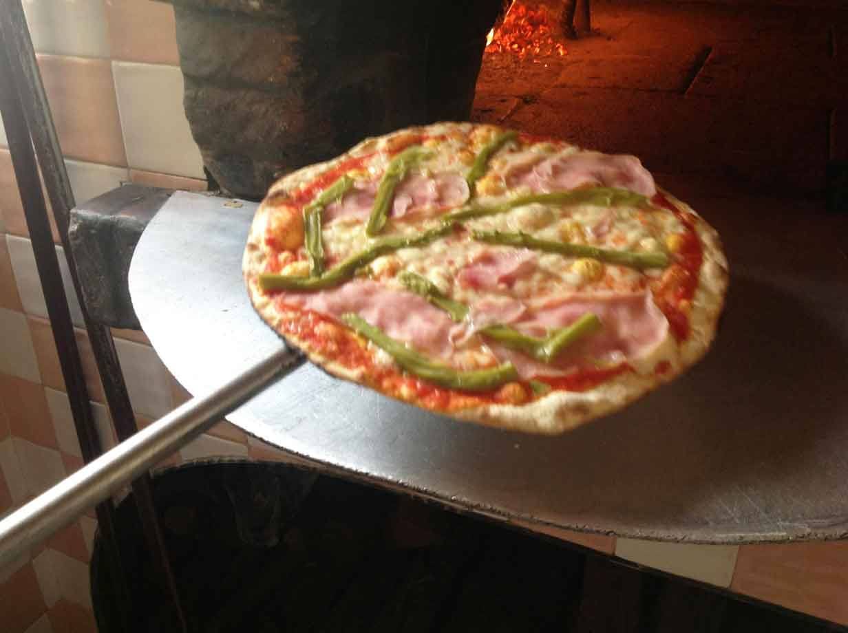 Pizza con prosciutto e peperoni sulla pala davanti al forno a legna