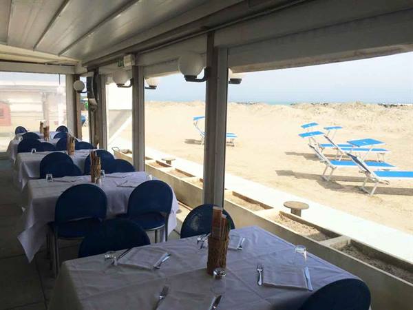 Restaurant dining room with set tables and blue chairs facing the beach