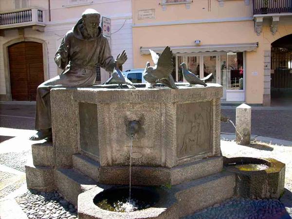 Bronze friar statue on a stone fountain with doves in a square