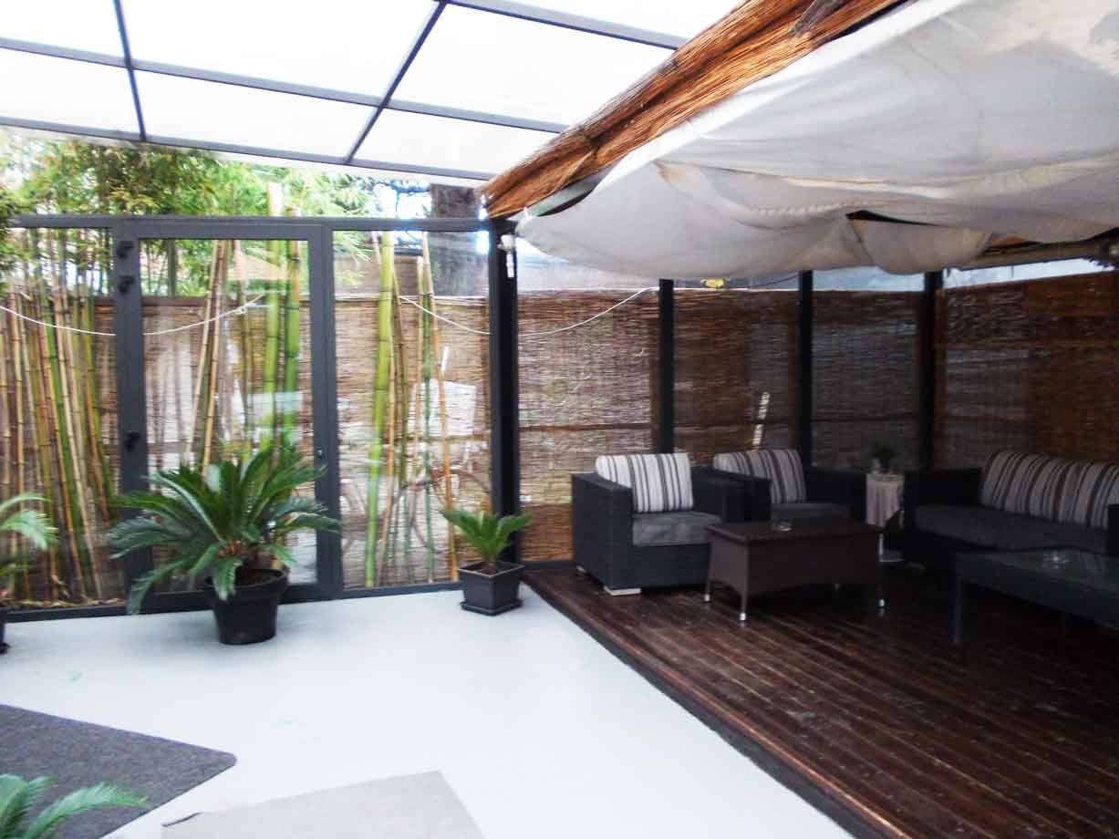 Terrazza coperta con divani scuri, pavimento in legno e bamboo