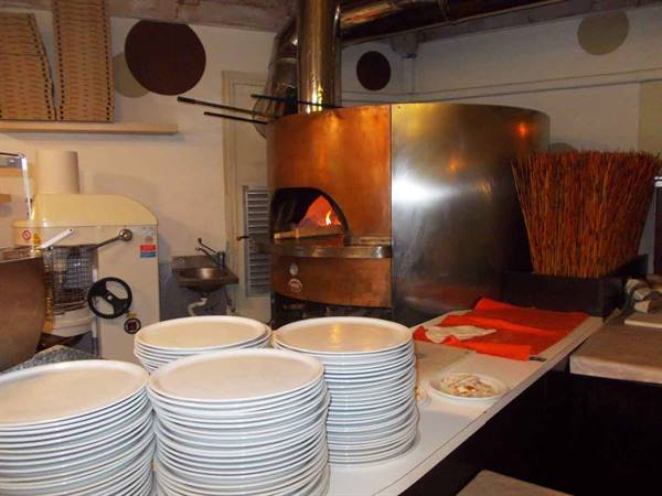 Steel and copper wood-fired oven lit, stacked plates on the pizzeria counter