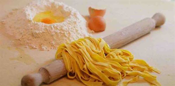 Fresh tagliatelle wrapped around a wooden rolling pin with eggs and flour
