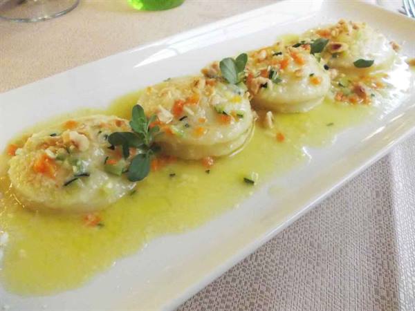 Four butter-sage ravioli with nuts and vegetables, served on white plate